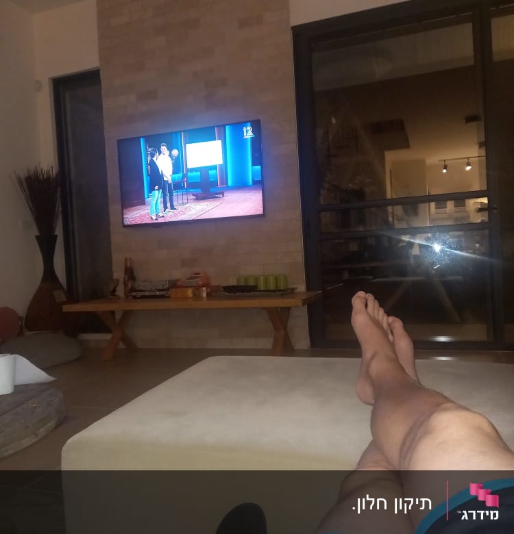 אדם יושב בסלון מול טלוויזיה דולקת